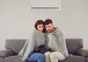 man and woman under a blanket on the couch because furnace is blowing cold air